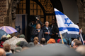 Präsidentin Grotheer steht im Eingang des Rathauses und spricht zu den Teilnehmer:innen der Kundgebung. Im Vordergrund ist eine wehende israelische Flagge zu sehen.