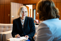 Dr. Imke Sommer sitzt im Präsidentinnenzimmer auf einem grauen Sessel und hat den ausgedruckten Bericht auf ihren Knien liegen.