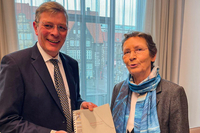 frank Imhoff und Bettina Sokol stehen nebeneinander im Präsidentenzimmer. Sie halten den Bericht zwischen sich und schauen in die Kamera. Durch das Fenster im Hintergrund sieht man den Marktplatz.