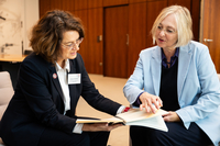 Dr. Imke Sommer sitzt im Präsidentinnenzimmer auf einem grauen Sessel neben Antje Grotheer und zeigt ihr den Bericht.