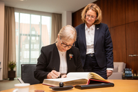 Lindita Nikolla sitzt am Besprechungstisch im Präsidentinnenzimmer und trägt sich in das vor ihr liegende Gästebuch ein. Antje Grotheer steht neben ihr und sieht ihr dabei zu.