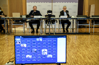 Martin Michalik und Dr. Carsten Sieling sitzen an Tischen in einem Raum. Vor ihnen sind auf einem Monitor die anderen Teilnehmer der Sitzung zu sehen.