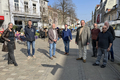 Die Mitglieder des Ausschusses stehen in einer belebten Straße im Viertel. Die Sonne scheint, im Hintergrund fährt eine Straßenbahn vorbei. Menschen sitzen draußen vor den Cafés.