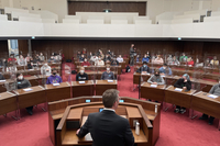 Frank Imhoff ist von hinten zu sehen, wie er am Redepult des Plenarsaals steht und zu den Schüler:innen spricht, die auf den Plätzen der Abgeordneten sitzen. Alle tragen Masken, auf den Pulten stehen Plexiglaskabinen.