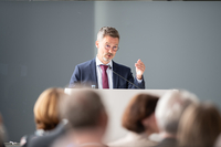Professor Spehrlich steht am Rednerpult im Festsaal. Vor ihm sind die Köpfe der Zuhörer:inne zu sehen.