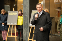 Frank Imhoff spricht bei der Aktion vor dem Haus. Er hält ein Mikrofon in der Hand und trägt einen schwarzen Mantel. Im Hintergrund sind Abgeordnete und Mitglieder von amnesty international zu sehen, die Schautafeln auf Staffeleien zeigen.