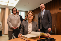 Die Botschafterin sitzt am Tisch und trägt sich in das Gästebuch ein, hinter ihr stehen Susanne Grobien und Frank Imhoff.