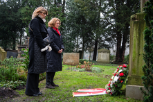 Sülmez Çolak und Antje Grotheer stehen auf dem Friedhof, vor ihnen auf dem Boden ist ein Kranz mit Schleife an einen Gedenkstein gelehnt.