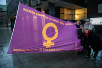 Antje Grotheer, Sahhanim Görgü-Philipp und Bettina Wilhelm halten die Flagge zum Aktionstag gespannt. Im Hintergrund ist das Haus der Bürgerschaft zu sehen. Der Boden ist nass vom Regen.