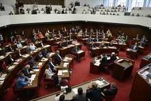 Die Abgeordneten sitzen an ihren Tischen im Plenarsaal. Die Zuschauertribünen oberhalb sind voll besetzt. Auf der Pressetribüne stehen mehrere Kamerateams und viele Journalisten.