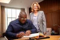 Joseph Uapingene sitzt am Koferenztisch im Präsidentinnenbüro und trägt sich in das Gästebuch ein. Neben ihm steht Antje Grotheer und sieht im dabei zu.