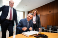 Der Generalkonsul sitzt am Besprechungstisch im Präsidentinnenzimmer und trägt sich in das vor ihm liegende Gästebuch ein. Die Präsidentin und der Honorarkonsul stehen neben ihm.
