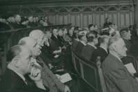 AUf den Bänken im Gerichtssaal sitzen viele Leute, fast ausschließlich Männer. Sie lauschen einem Redner außerhalb des rechten Bildrands.