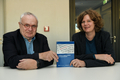 Henning Lühr und Ulrike Peter sitzen in einem Besprechungsraum nebeneinander an einem Tisch und schauen in die Kamera. Henning Lühr hat graue Haare, er trägt eine Brille und ein schwarzes Sakko. Ulrike Peter hat braune Haare und trägt einen schwarzen Blazer. Zwischen sich halten die beiden aufrecht ihr neues Buch in die Kamera.